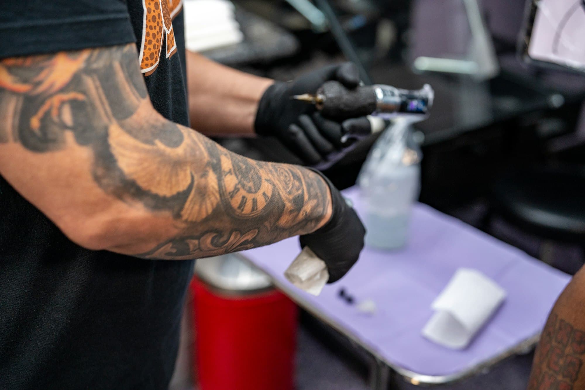 Un avant-bras tatoué et des mains gantées préparant le matériel avant une séance.
