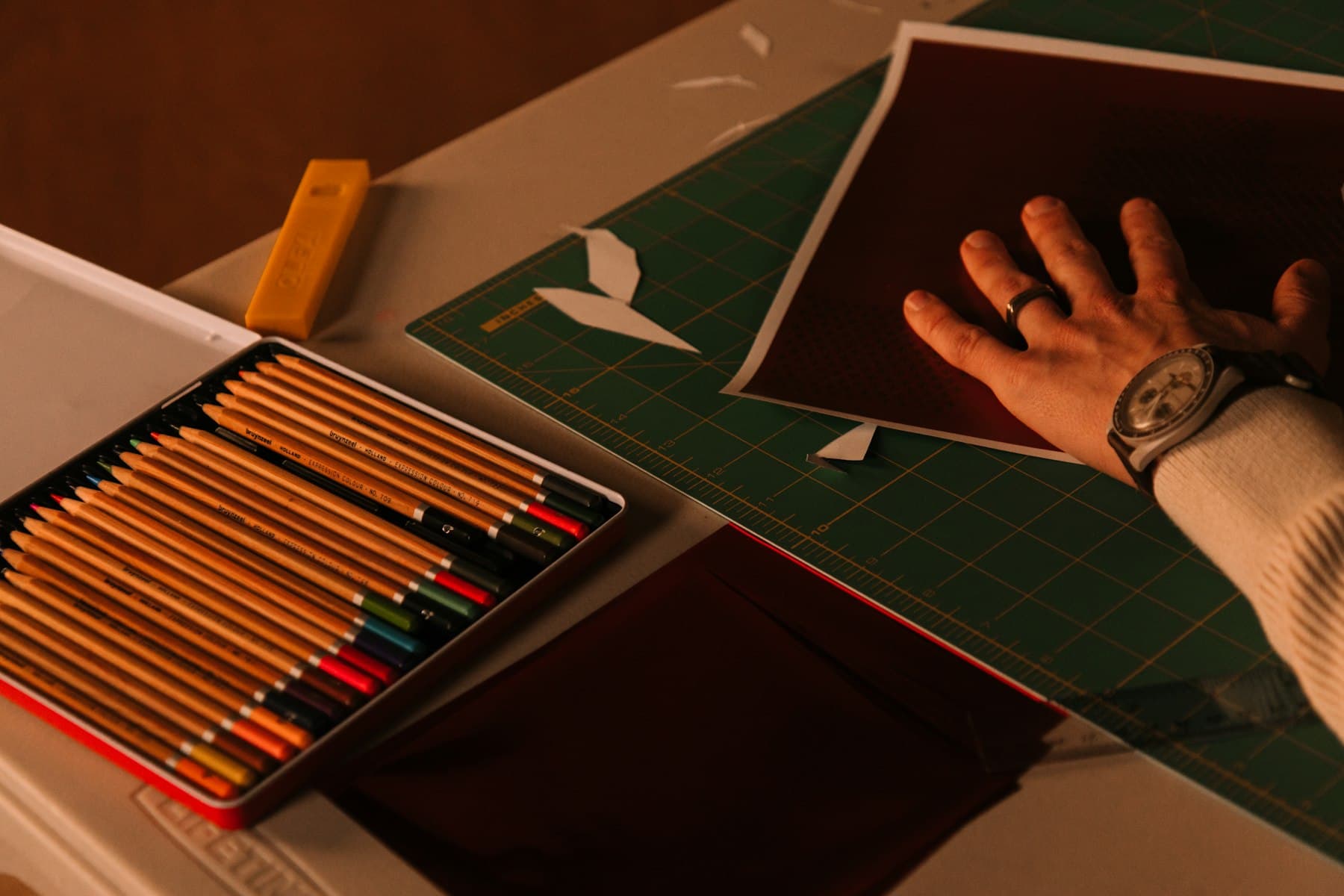 Une table de dessin : crayons de couleur, papier découpé, tapis de coupe.
